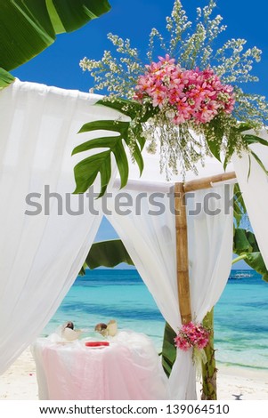 wedding arch and set up with flowers on tropical beach under palm trees