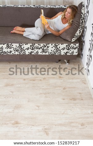 A woman reading a book and smiling as she lays on sofa in room
