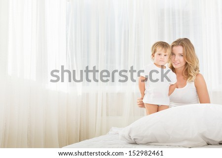 indoor portrait of young happy mother and baby child in bed at home in the morning