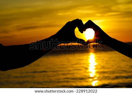 young loving couple on wedding day on tropical beach and sunset sea background, heart shaped figure made by hands