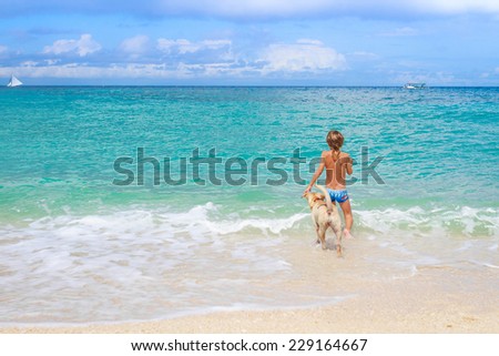 young happy child boy having fun with white dog in the sea, summer vacations