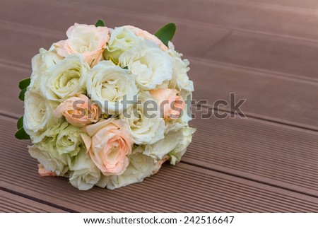 Wedding bouquet of peach and white roses lying on wooden floor