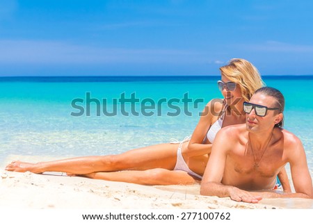 Beach couple looking. Happy young couple lying on sand under sunny summer sun. Travel holidays concept