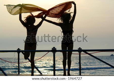 silhouettes of two young girls with scarfs dancing on a bridge at sunset