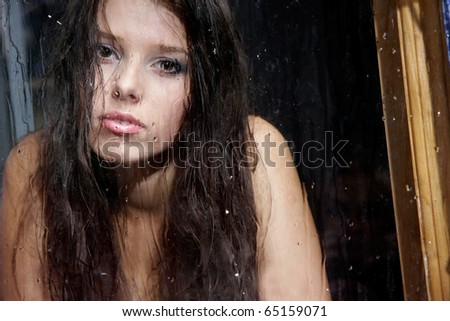 young sad girl behind wet window