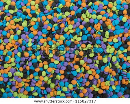 Background of colorful candy sprinkle toppings.  Round shapes in orange, black, purple, blue and green.