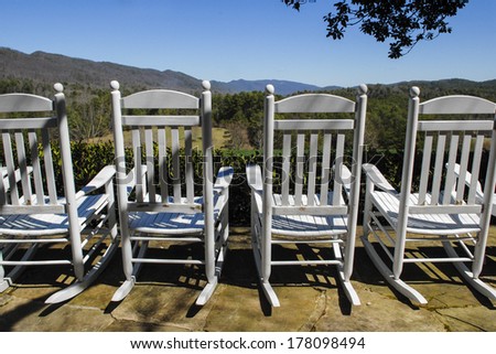 White rocking chairs overlooking rolling mountain hills on a blue sky day