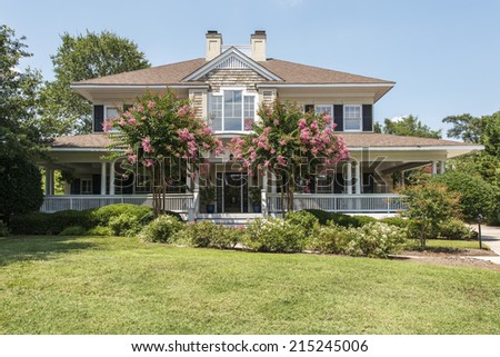 Gorgeous southern home with wrap around white porch and blooming crepe myrtle trees