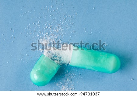 Opened Green Pill Capsule with contents spilled out on blue background