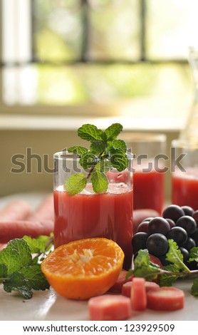 Fresh red carrot juice surrounded by fresh fruits and vegetables and mint leaves