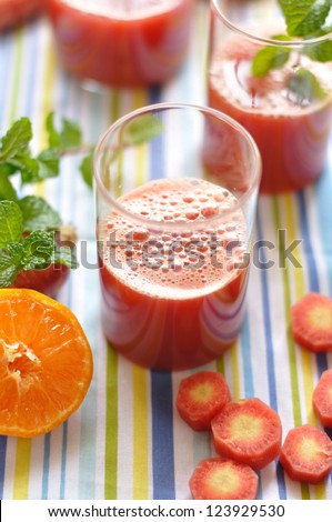 Fresh red carrot juice surrounded by fresh fruits and vegetables and mint leaves