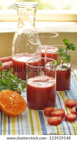 Fresh red carrot juice being poured surrounded by fresh fruits and vegetables and mint leaves