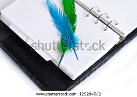 A diary or notebook isolated on the white background with a couple of colorful feathers