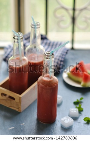 Watermelon juice in a soda bottle with straw and sliced watermelon in background on a blue background
