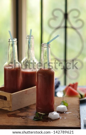 Watermelon juice in a soda bottle with straw and sliced watermelon in background on a blue background