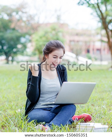 female student sitting on the green field and exciting with laptop computer