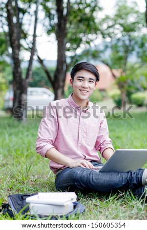 Young man student sitting on the grass and work with laptop computer