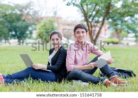 female and male students sitting on the green field with laptop computer and books