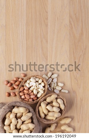 Peanuts in the bag sack and baskets with empty space on wooden background