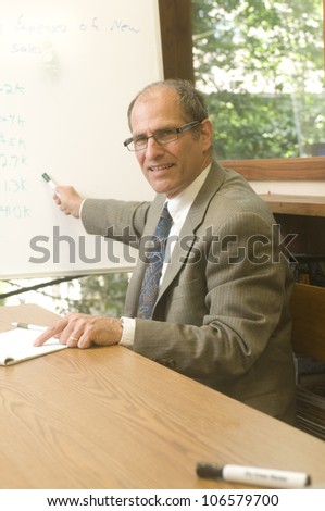 senior business executive in conference office giving presentation with sales figures on display board