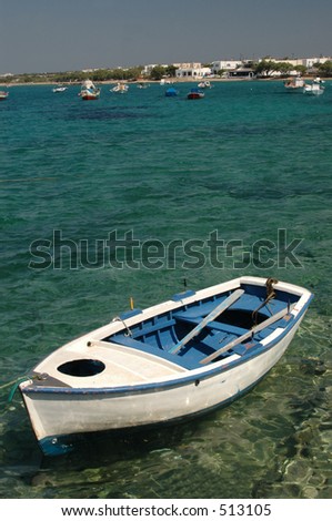 an old wood row boat in the harbor with hotels in the distance in the greek islands