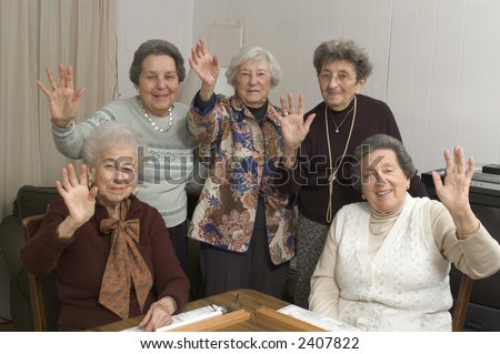 group of happy senior women playing mah-jong with friends waving hello