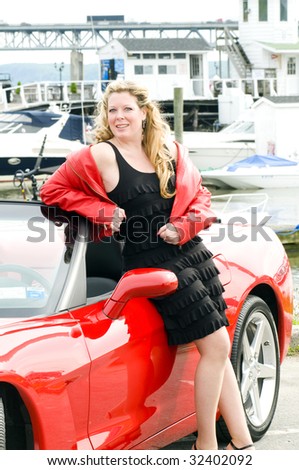sexy woman smiling with hot red convertible sports car in front of yacht club boats on river
