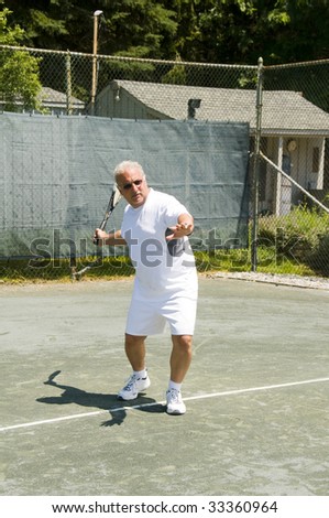 handsome middle age male tennis player hitting forehand stroke on tennis court at club
