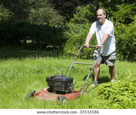 handsome middle age man cutting overgrown grass with old fashioned lawn mower at suburban house