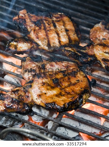 thin center cut bone in pork chops cooking on a charcoal barbecue grill with grill marks and hot coal flames