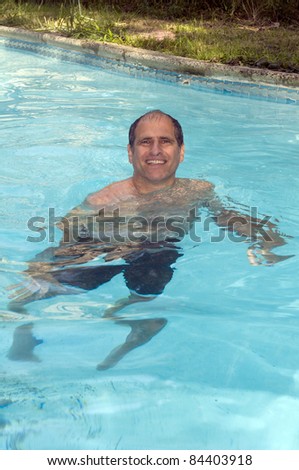 handsome smiling middle age man swimming in suburban house private swimming pool