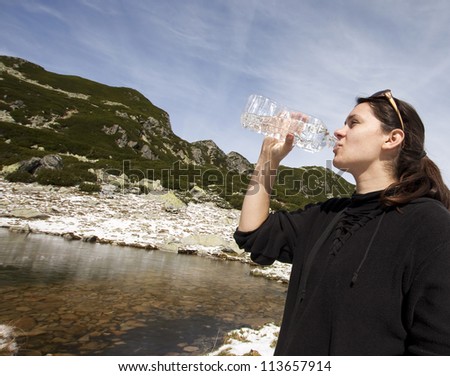 Woman drinking crystal clear water from bottle in mountain scenery