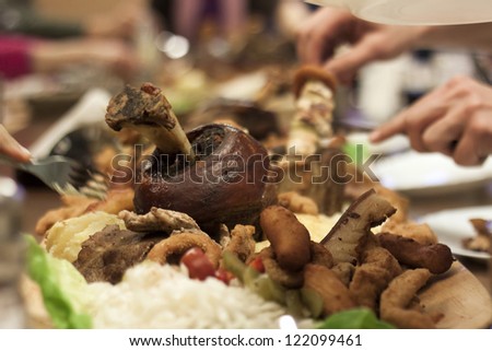 People serving from big platter with all kind of fried meat and roasted pork knuckle