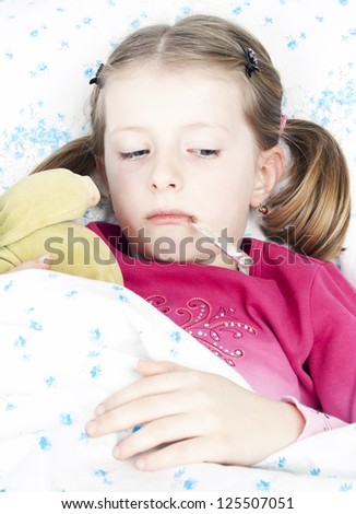 Sick girl with a thermometer and teddy bear lying in bed