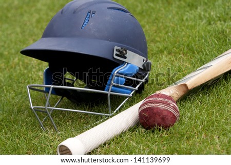 Cricket ball, bat and helmet on green grass of cricket pitch