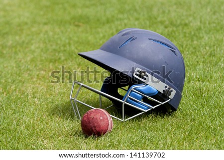 Cricket ball, bat and helmet on green grass of cricket pitch