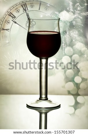 Red wine against fireworks, holiday lights and clock close to midnight