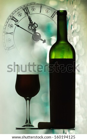 Glasses and bottle of red wine against holiday lights and clock close to midnight