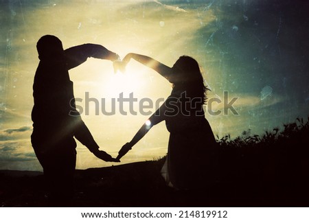 Silhouette of loving couple holding hands in heart shape over orange sunset background - vintage photo