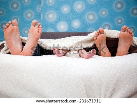 Three pairs of legs of the happy family in bed - father, mother and baby