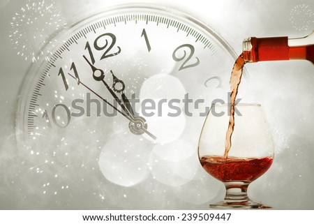Pouring red wine against fireworks and clock close to midnight