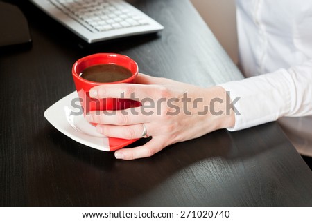Woman hands on red cup of coffee on an office table