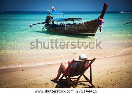 Exotic beach holiday background with woman sitting in  beach chair and long tail boat - Thailand ocean landscape