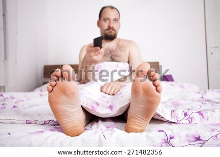 Man watching TV from the bad - close up on the feet