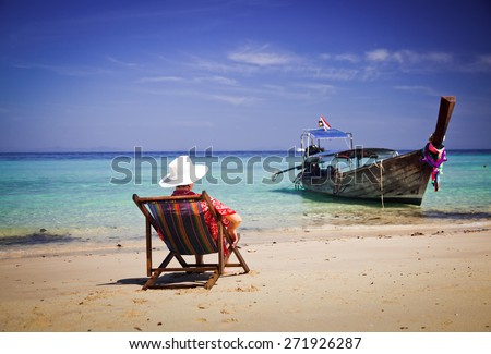 Exotic beach holiday background with woman sitting in beach chair and long tail boat - Thailand ocean landscape