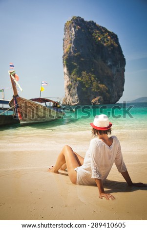 Woman sitting on Tropical beach relaxing and watching longtail boats, Andaman Sea, Thailand