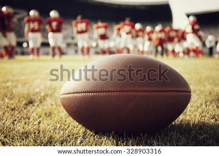 Close up of an american football on the field, players in the background - retro styled photo