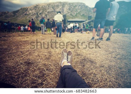 Teens at concert at summer festival. Legs of teenager at summer music festival, canvas shoes, sitting on the grass in front of stage