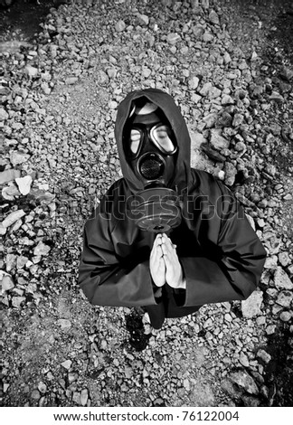 Man with gas mask praying in desolated land with ruins and pipes