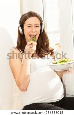 pregnant woman eat salad and listening to music